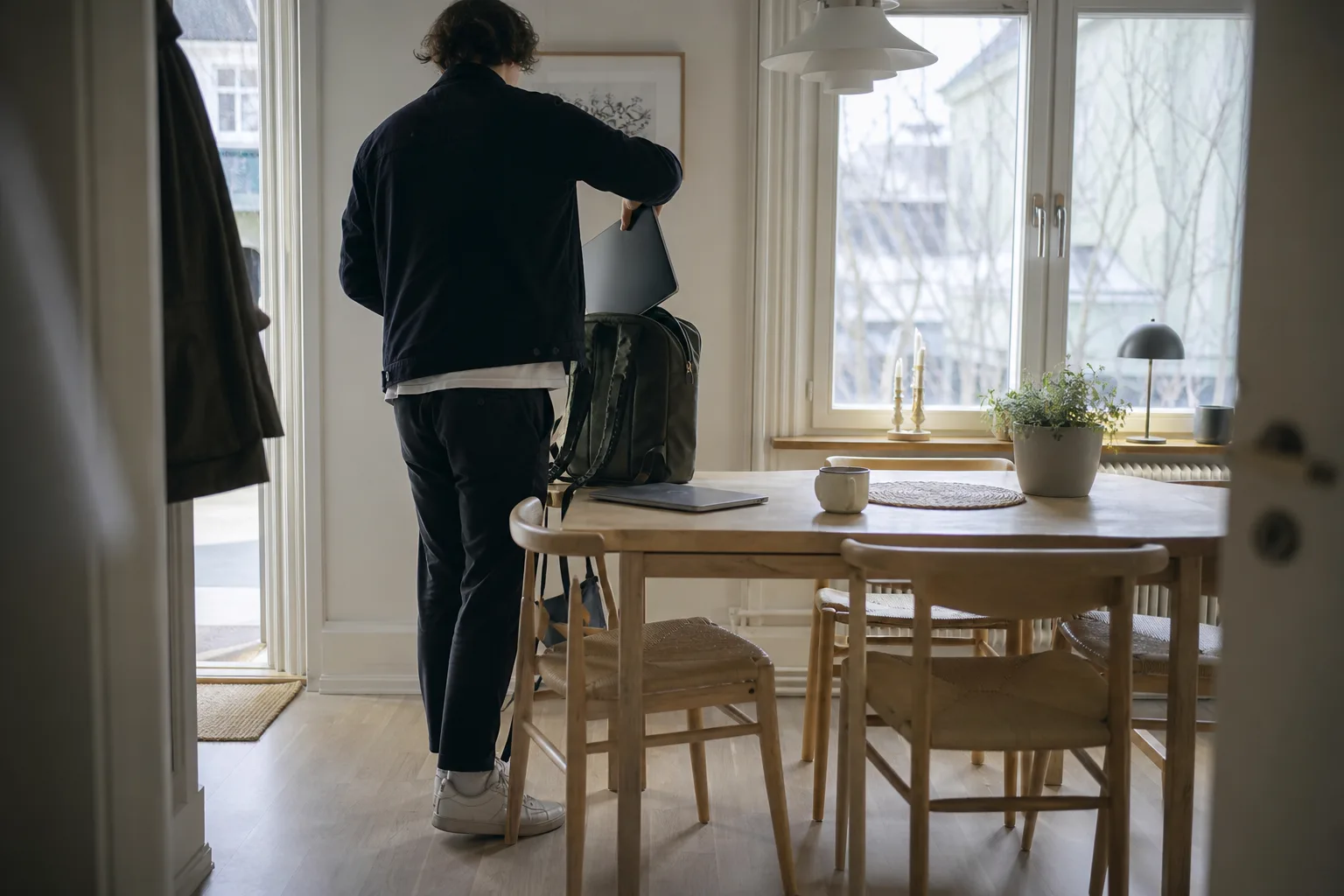 Person bakifrån lägger en tunn skärm i en ryggsäck bredvid en bärbar dator