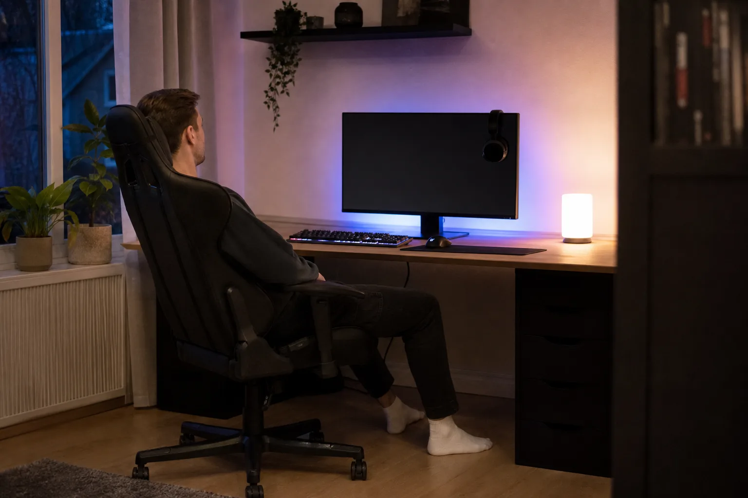 Person sedd från sidan sätter sig i en gamingstol framför en avstängd skärm med headset