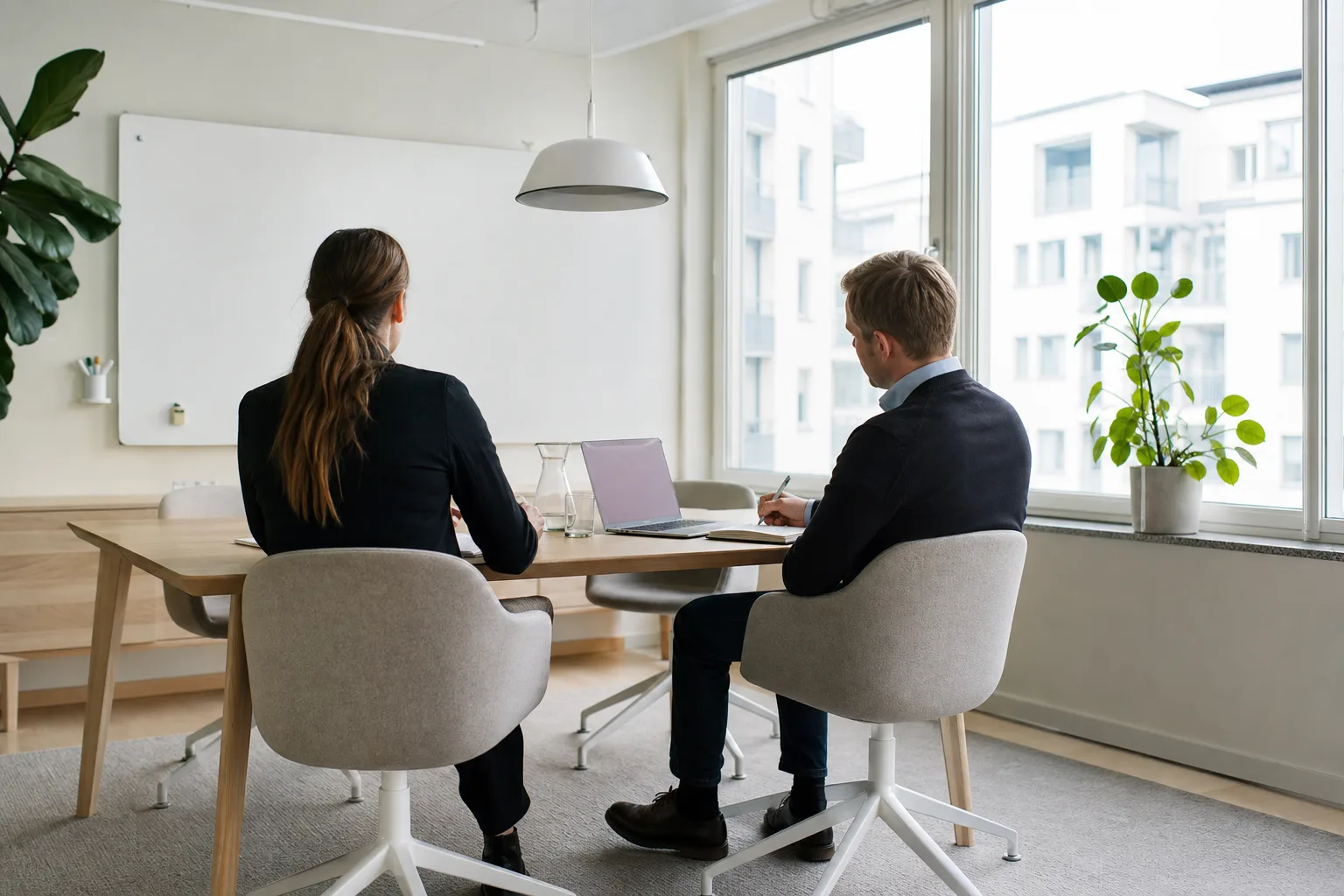 Två personer bakifrån och från sidan går igenom anteckningar vid ett bord i ett mötesrum